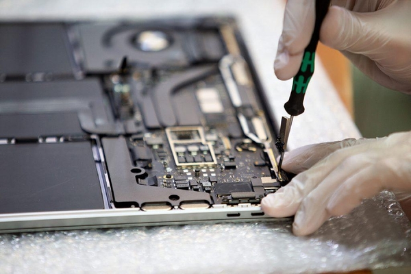 Fachmann löst eine Schraube beim Logicboard-Austausch - filigrane Arbeiten am MacBook